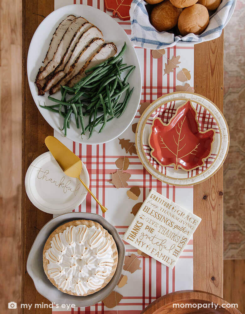 Thanksgiving dining table set up with My Minds Eye - Harvest Thanksgiving Plaid Round Plates layered with maple plates, with Harvest/Thanksgiving Mini Leaves Banner cross through Thankful small paper plates, Harvest/Thanksgiving 7" Luncheon Napkin, bread in the basket, pie, turkey and veggies in the plate, on top of Harvest/Thanksgiving Plaid Table Runner. These warm tone with plaid texture design and a touch of gold, are prefect stress free party supplies to your thanksgiving holiday table