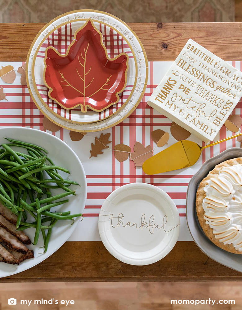 clost up Thanksgiving dining table set up with My Minds Eye - Harvest Thanksgiving Plaid Round Plates layered with maple plates, with Harvest/Thanksgiving Mini Leaves Banner cross through Thankful small paper plates, Harvest/Thanksgiving 7" Luncheon Napkin, bread in the basket, pie, turkey and veggies in the plate, on top of Harvest/Thanksgiving Plaid Table Runner. These warm tone with plaid texture design and a touch of gold, are prefect stress free party supplies to your thanksgiving holiday table