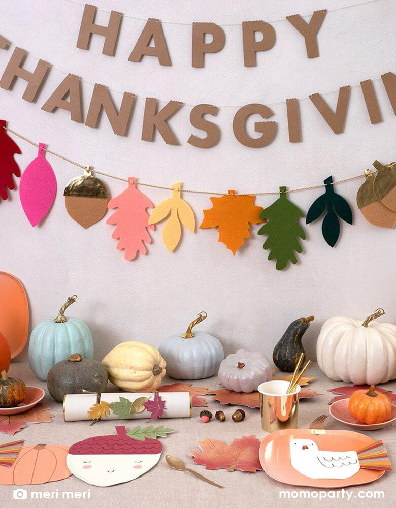 Thanksgiving party idea with Meri Meri Felt Leaves Thanksgiving Garland hanging on the wall, there is pastel pumpkin plates with Thanksgiving Fringed Turkey Napkin, Maple Leaf Napkins, Pastel Halloween Pumpkin Napkins, acron napkins on the table, a gold foil tumbler with gold straw, lots of pumpkin decorations as centerpiece. They are super fun for festive Thanksgiving celebration, fall party, Harvest party. find these high end thanksgiving party supplies at momoparty.com