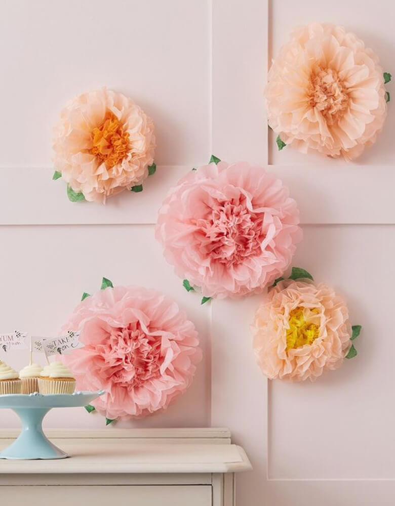 Ginger Ray Tissue Paper Pompom flower decoration backdrop in blush, pastel pink and peach, hung on the wall beyond the dessert bar with cupcake topped with "Tea Time" toppers for an afternoon tea party. It makes a great decoration for a garden party, girl's butterfly fairy birthday, girl's baby shower, bridal shower or an Easter celebration