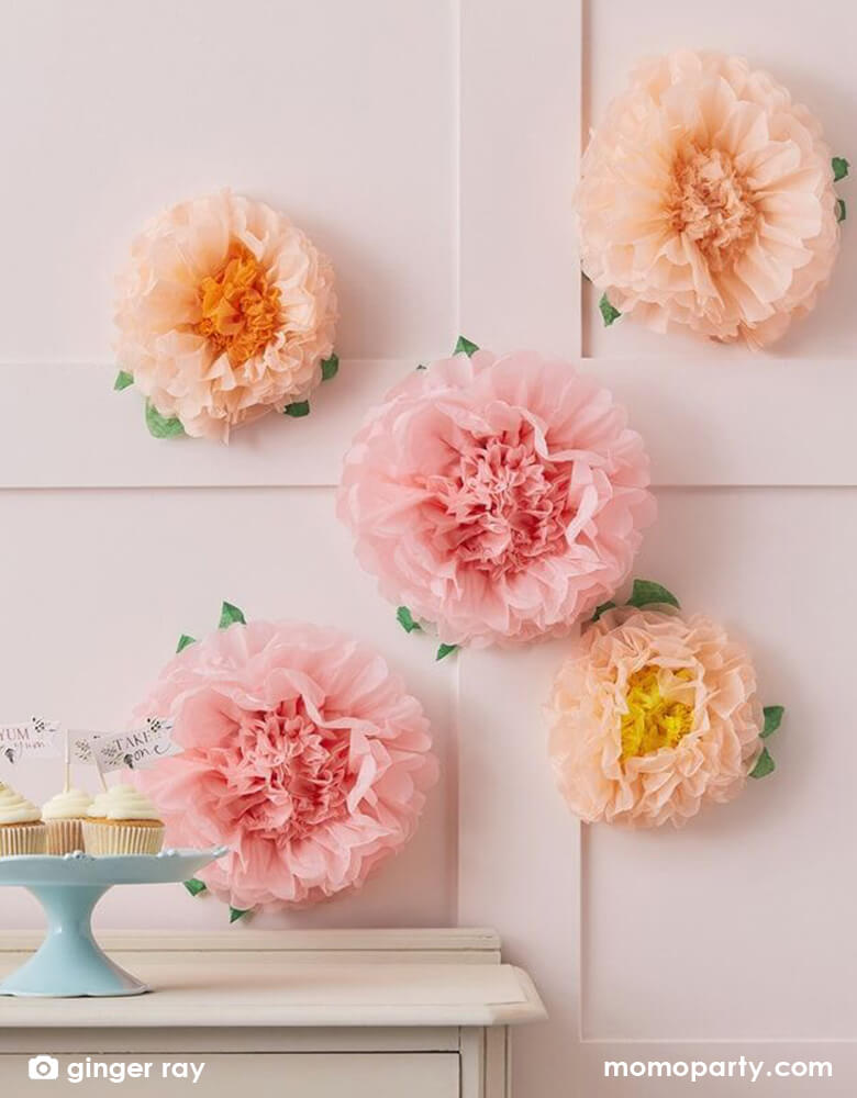 Ginger Ray Tissue Paper Pompom flower decoration backdrop in blush, pastel pink and peach, hung on the wall beyond the dessert bar with cupcake topped with "Tea Time" toppers for an afternoon tea party. It makes a great decoration for a garden party,  girl's butterfly fairy birthday, girl's baby shower, bridal shower or an Easter celebration 
