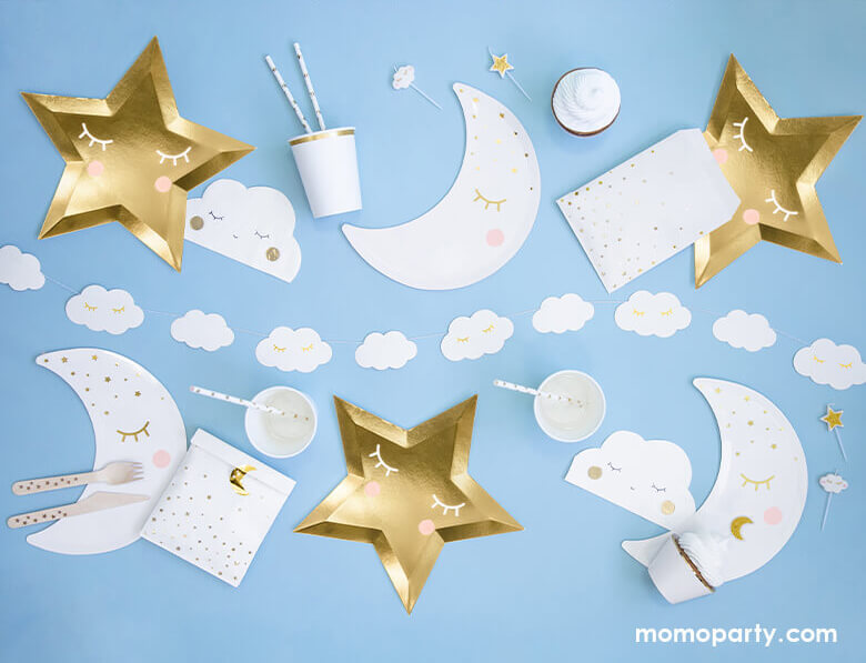 A flatlay shot of a baby blue table setup for a sweet baby boy shower filled with sweet Star themed party goods including die cut gold star plates, little cloud napkins in white, moon shaped plates in white with pink party cups and Little Cloud banner in the center, cupcakes and party bags.