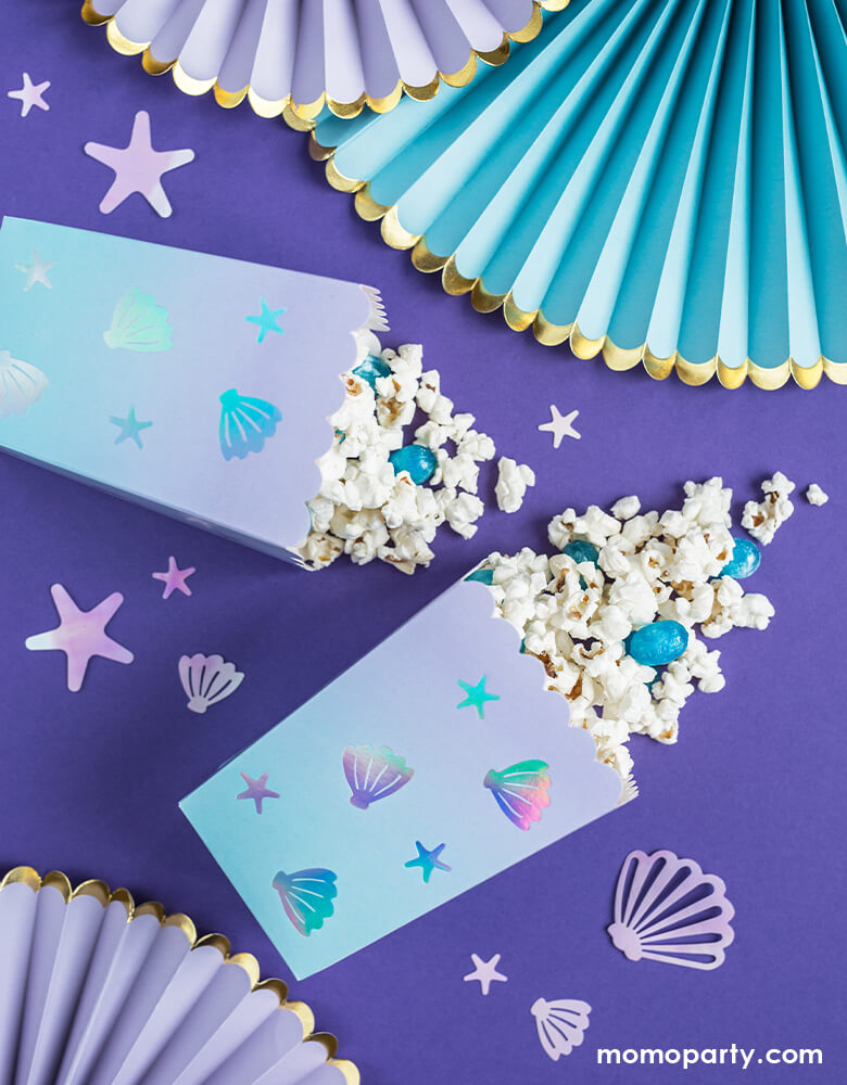 Under The Sea party table with Popcorns and blue jelly beans out from Party Deco Under The Sea Popcorn Treat Boxes, Decorative Rosettes Yummy party paper fans, Mermaid Narwhal Iridescent Confetti over lilac tablecloth