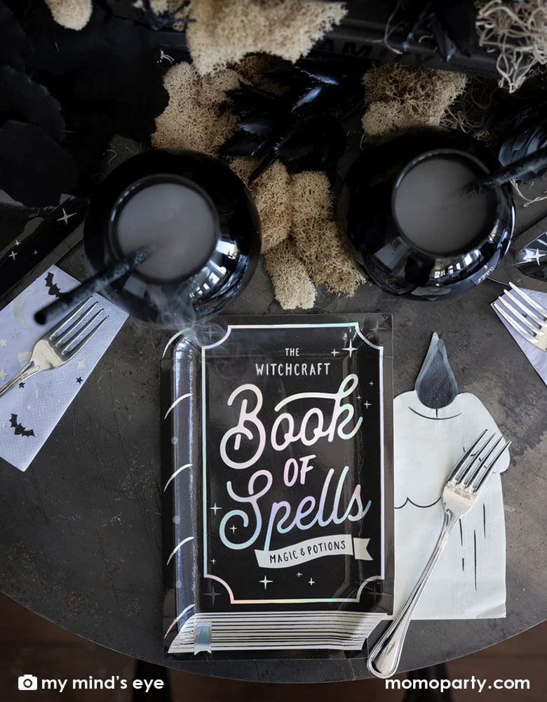 A Halloween witch themed party table filled with witch inspired tableware including My Mind's eye witch hat shaped plates, book of spells shaped plates, lilc witching hour small napkins and cauldrons for witch brew