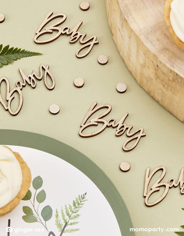 Modern baby shower table close up with cupcake on a BOTANICAL HEY BABY SHOWER PLATES, with Ginger Ray - Wooden Baby Confetti on the Pistachio colored table cloth. This Wooden Baby Confetti Contains 18 Wooden Confetti Pieces of "baby" script shape and small circle pieces. Scatter your table with this wooden baby shower confetti to compliment a natural baby shower table decorations.