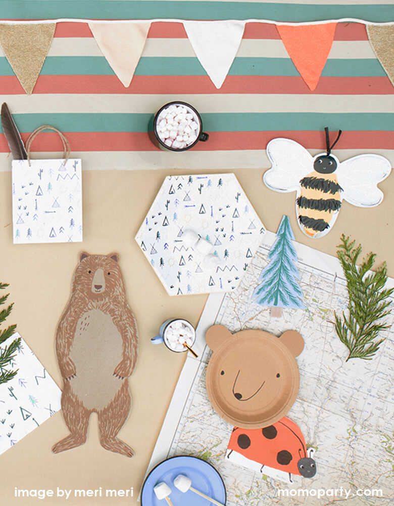 Woodland Camping party tabletop filled with Meri Meri Bear Small Plates, Ladybug Napkins, Meri Meri Bee Plates, Brown Bear plate, Let's Explore Large Plates napkin and cups, Let's Explore party bag with a feature inside, Bee plates, a small cup of hot chocolate with marshmallow, color stripe tablecloth with mini flags, enjoy the fun with this modern look and fun designed woodland camping party for your summer night camping party