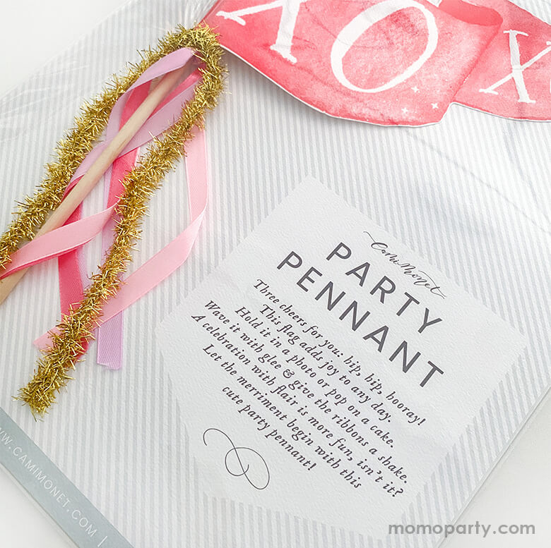 Close up of Cami Monet - XOXO Party Pennant in package and usage information . This Handmade pennant made in United States of America, in Size: 10 x 5 inches. This is made of 120 lb. luxe watercolor texture paper with handwriting "XOXO" text in watercolor illustration for extra whimsy. With pink and red and gold mixed Ribbon and sparkle garland. This adorable party pennant is a perfect for a sweet Valentine's Day celebration!