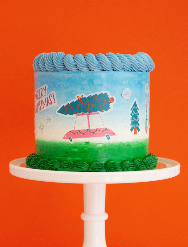 Gif image with a blue white and green buttercream cake on a white cake stand, decorated with Make Bake shop Let's Get A Tree! Cakescape Edible Stickers with a truck carry christmas tree, snowflakes, "merry christmas" sign, many kinds of trees designs. These easy baking hacks cakescape edible stickers so easy to make decorating holiday cakes so much easier!