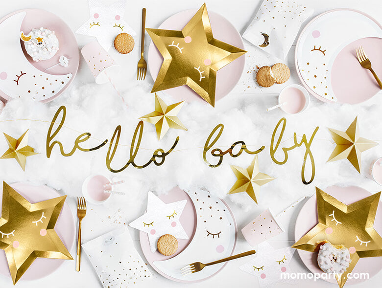 Baby Shower table set up with sweet Star themed party goods including die cut gold star plates, little star napkins in white, moon shaped plates in white with pink party cups, party favor bags and a gold garland with "hello baby" spelled out