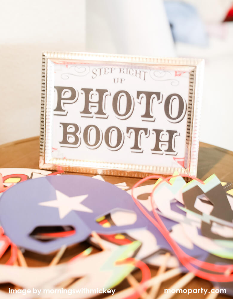 a corner of a superhero party table with a Photo Booth sign and My Minds Eye - Paper Love Comic Pop Photo Props, ready for some fun superhero party activities 